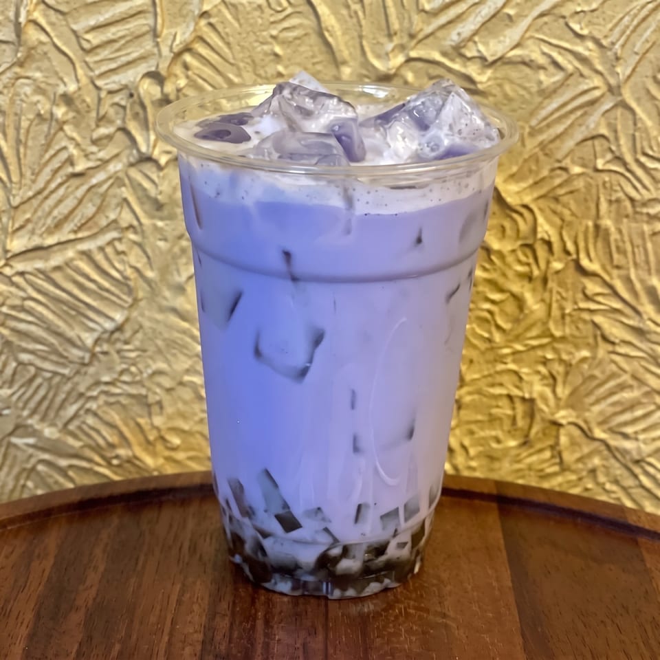 Purple iced beverage with jelly pieces and whipped topping in a clear cup on a wooden table.